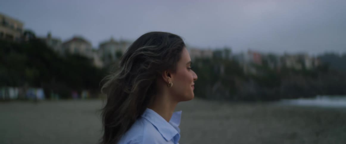 A woman smiles as she stands on a beach looking out at the water