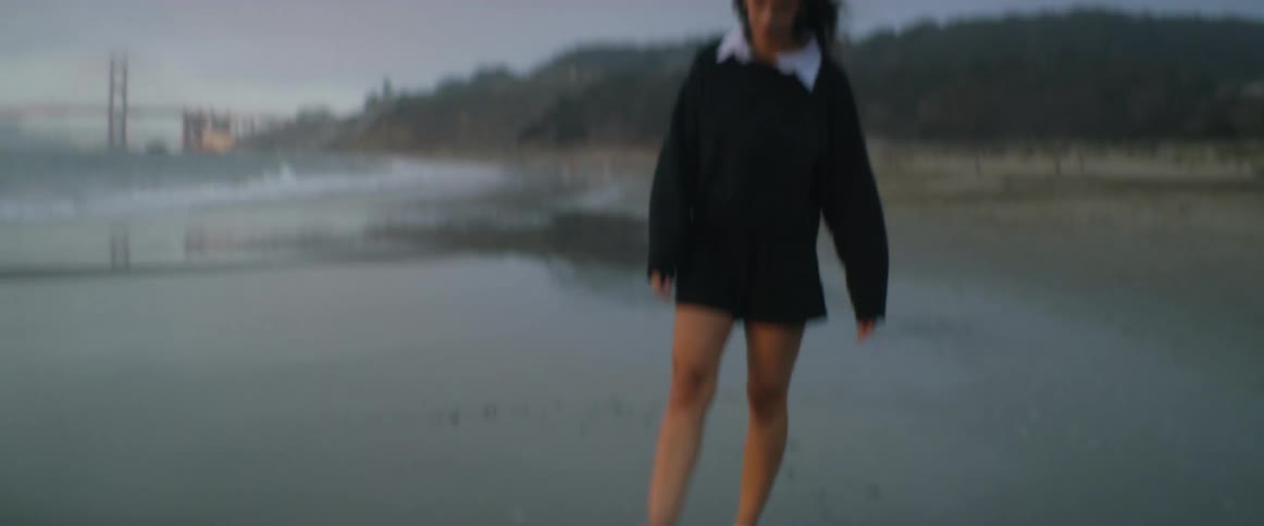 A young woman walks along the beach as waves roll in