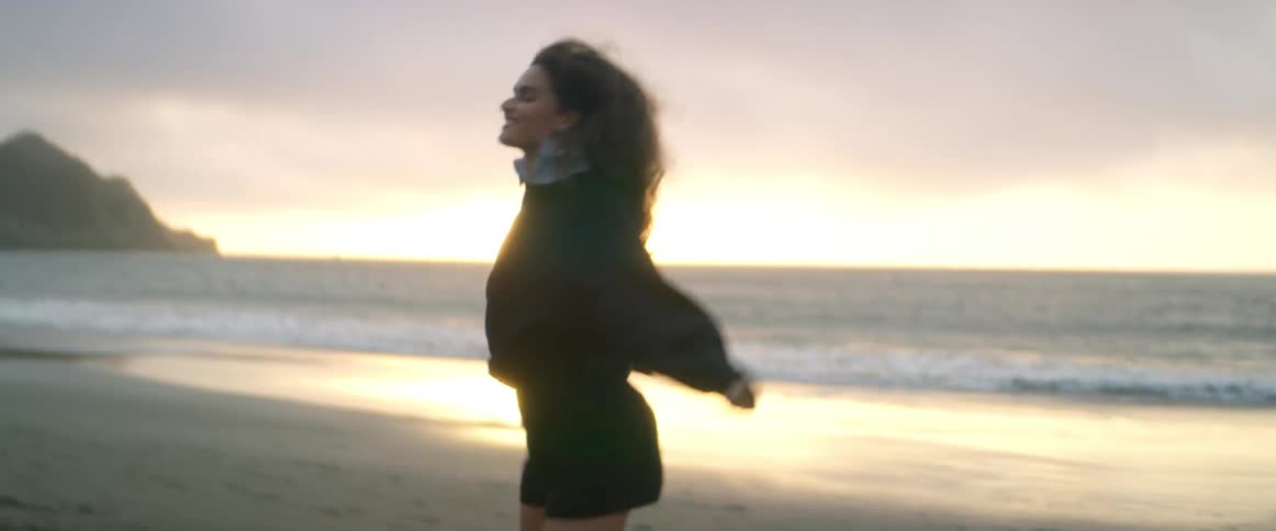 A happy woman is walking and dancing on a beach as the waves roll in