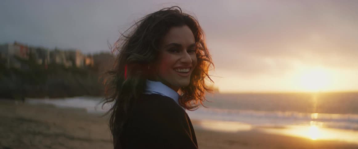 A woman is standing and laughing on an ocean beach at sunset