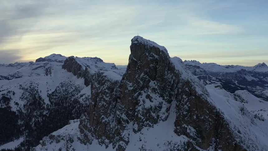 Aerial view of high snowy mountain with summit cross on top of it at dusk