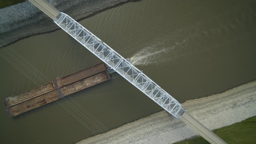 Top down view of cargo barges traveling upriver under a steel bridge