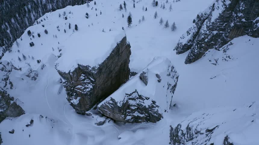 A large rock formation on the slope of a mountain covered in snow in the evening