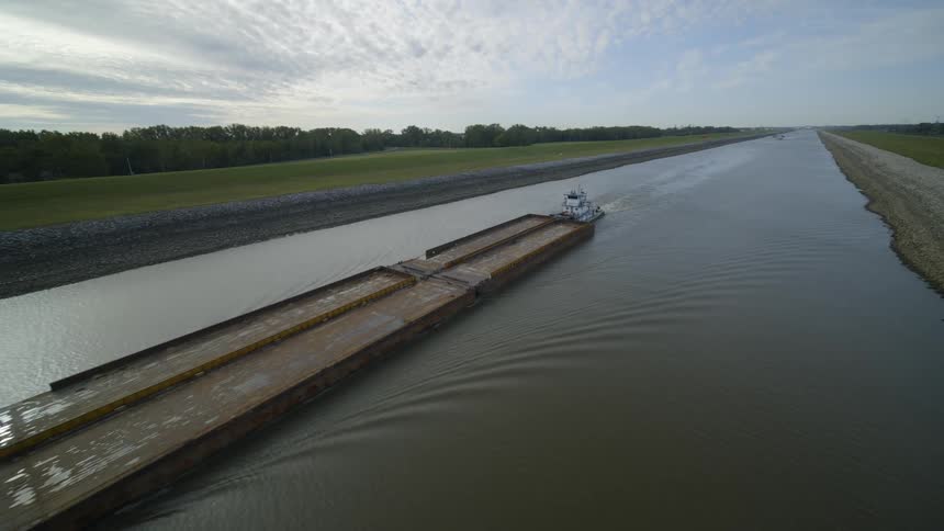 Pullback reveal over a long cargo barge as it travels along an inland waterway