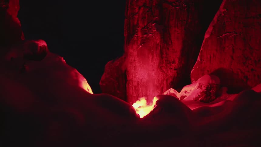 A burning campfire at night causes surrounding rock formations to glow red