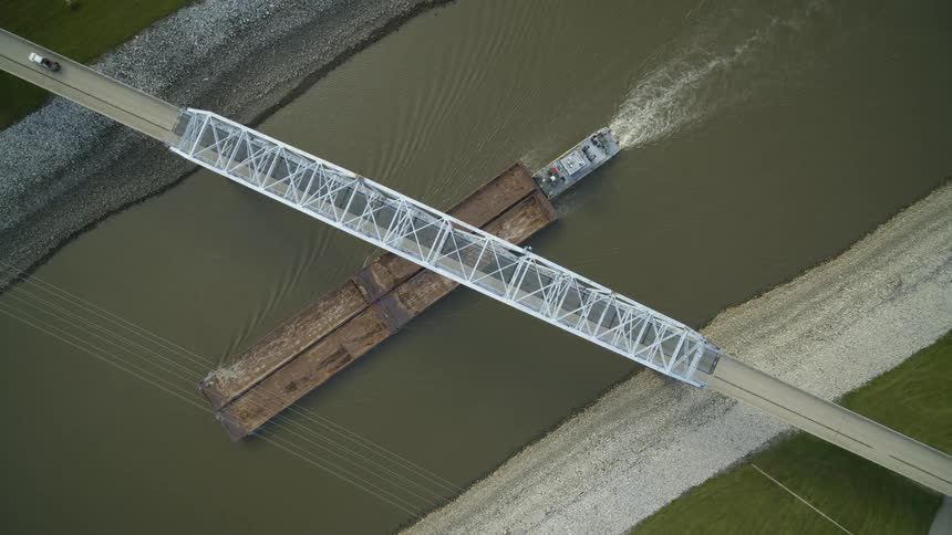 Subtle overhead twist as a barge passes under a bridge with a truck driving on it