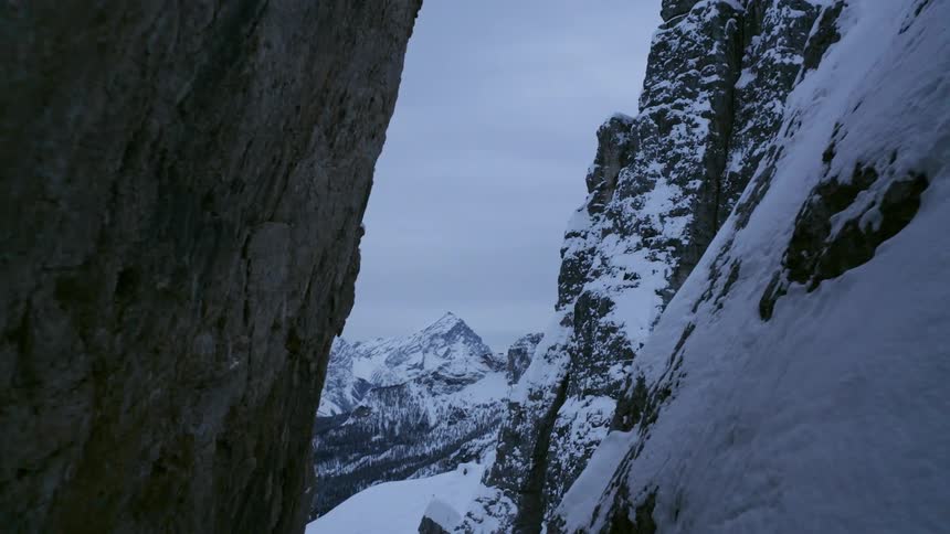 A cliff covered with snow and ice with a mountain range the sky and clouds in the background
