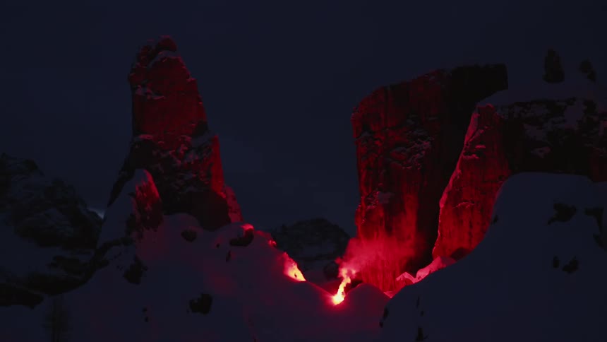 A fire and smoke near a cliff with snow with the sky and clouds in the background