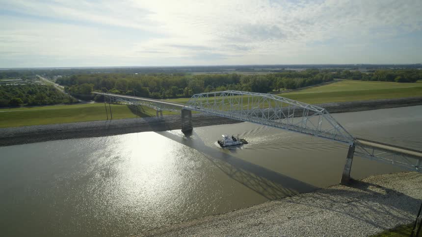 A towboat passes under a steel bridge traveling along a canal