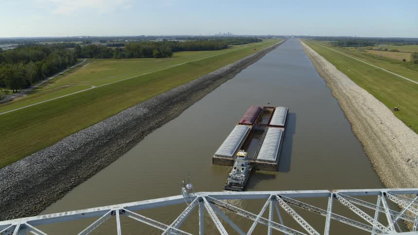 A freight barge travels downriver towards a city skyline in the distance