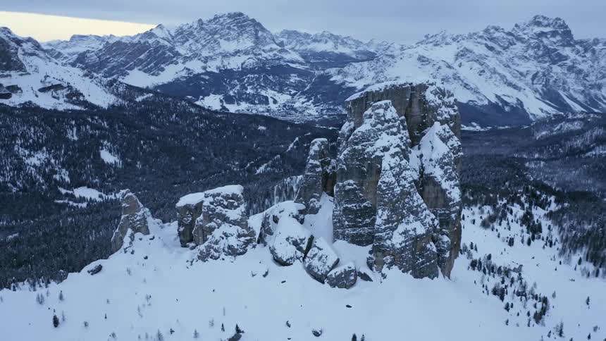 A rock formation sits on a hill near snow covered mountains