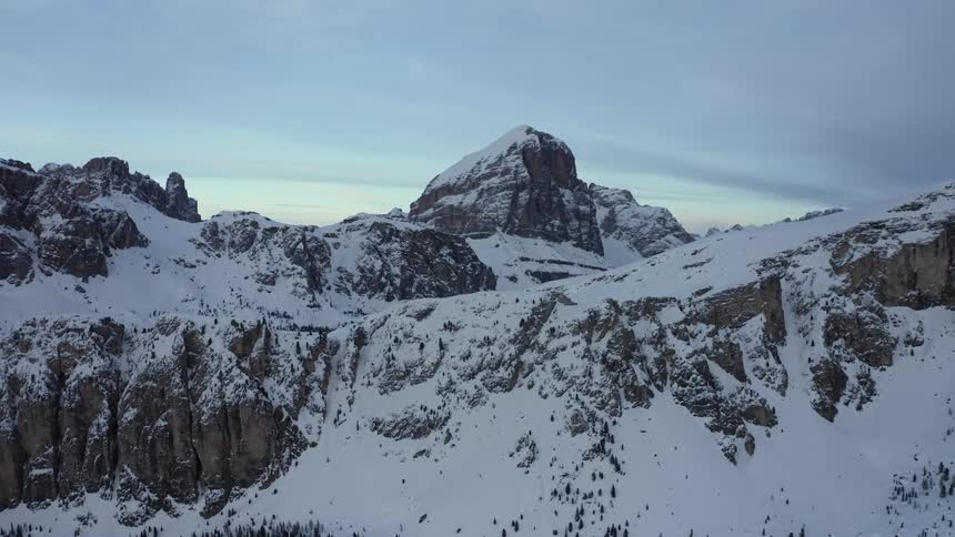 Snow covers conifer forest in valley and mountain range under cloudy sky