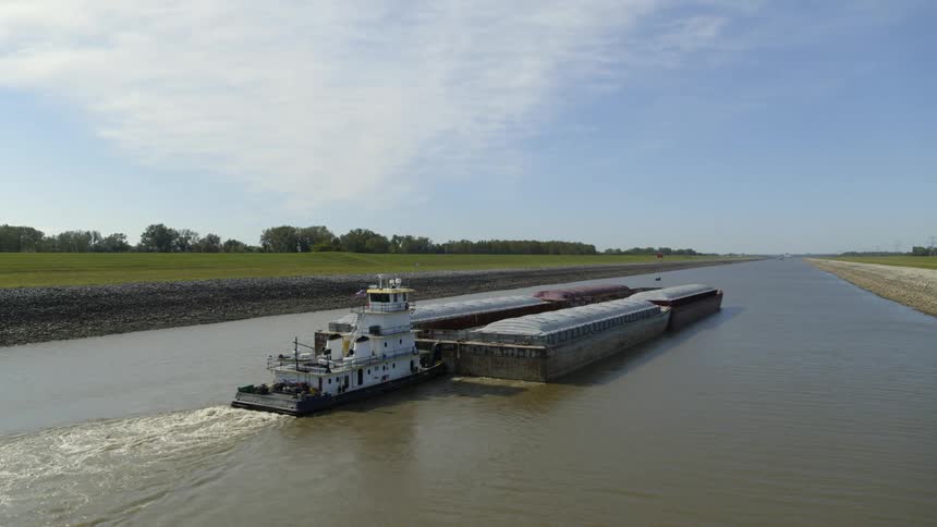 Approaching low behind a cargo barge as it travels through a narrow inland waterway