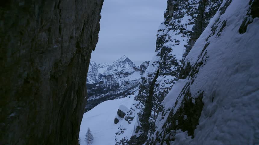 Snow covers just one side of a slope where two mountains closely meet
