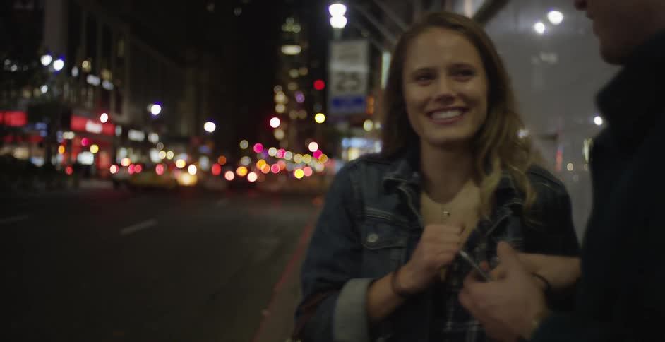A man and woman talk on the sidewalk of a city at night