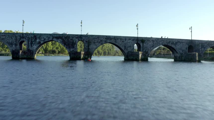 Aerial virw of a person inside a red kayak on a river next to a bridge at morning
