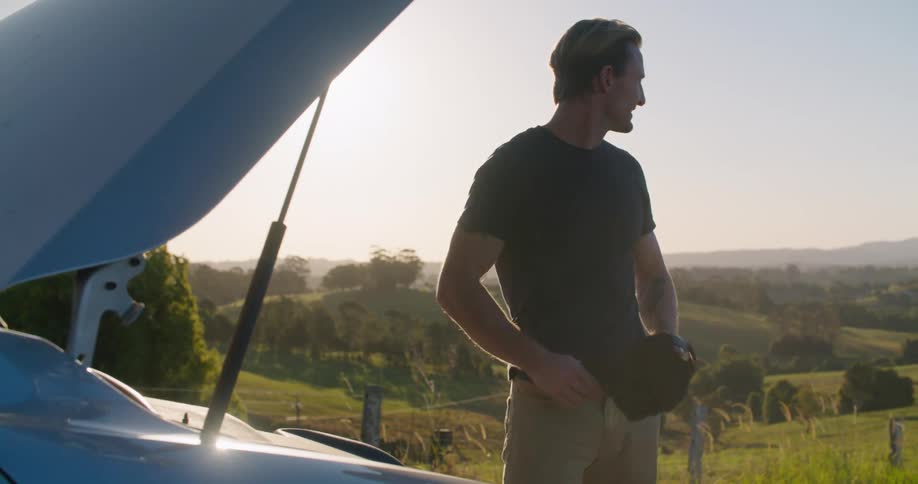 A man takes his hat off in frustration after look under the hood of his broken down vehicle