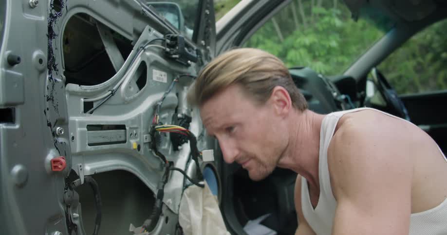 A man kneeling before an open car door uses a torque wrench to tighten bolts on the interior of the door