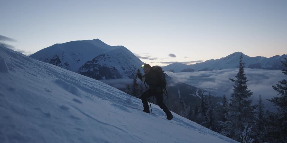Man hikes up steep snow covered mountain slope