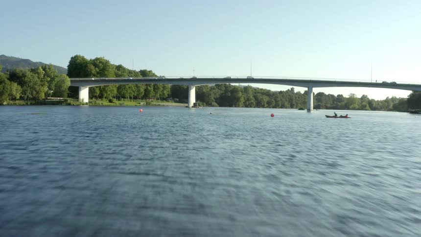 Small boats are in the water as cars travel across a bridge over the river