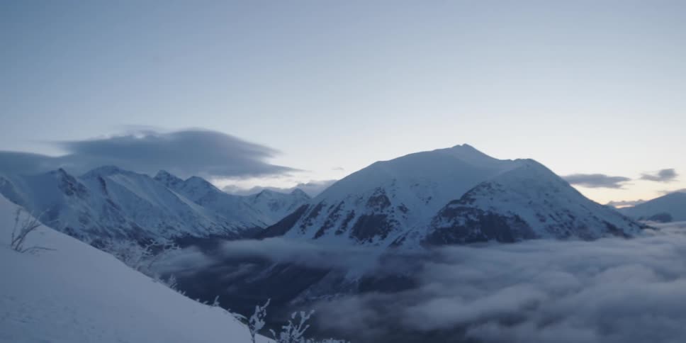 A hiker standing on the slope of a mountain looks out over the snowy landscape in the distance