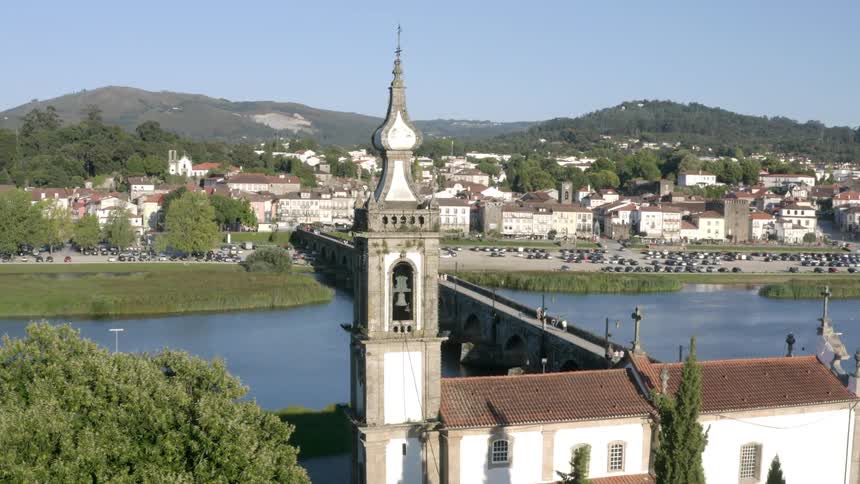 A building with a bell tower and a spire and a bridge crossing the river where there are many buildings