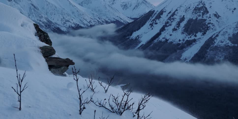 Wind is blowing a snowball down a hill on top of snow covered mountains