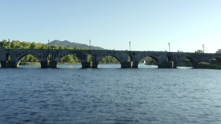 A person walks across a bridge as another person paddles a boat underneath