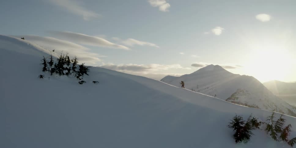 A person is hiking with poles up a snow covered mountain ridge at sunset