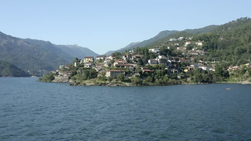 An aerial view of a large lake surrounded by forested mountains with a small town on a hazy day