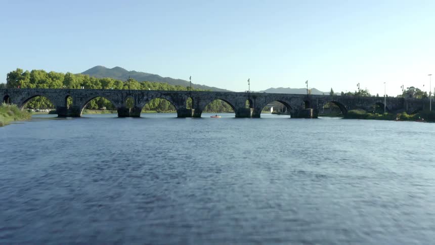 A river with a bridge with trees the sky and clouds in the background