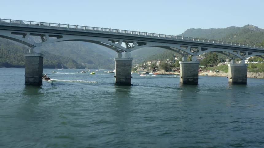 A motor boat passes under the arches of a bridge joining other boats racing away from shore