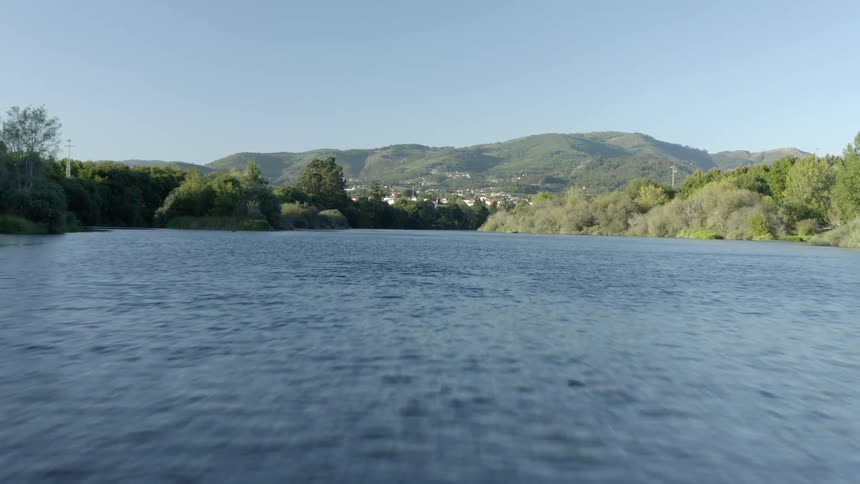 A lake is surrounded by trees and mountains in the distance under a clear blue sky