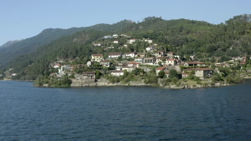 A coast with trees buildings and hills with the sky and clouds in the background