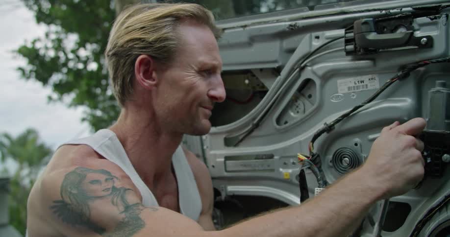 A man sits on the ground and fixes his car door