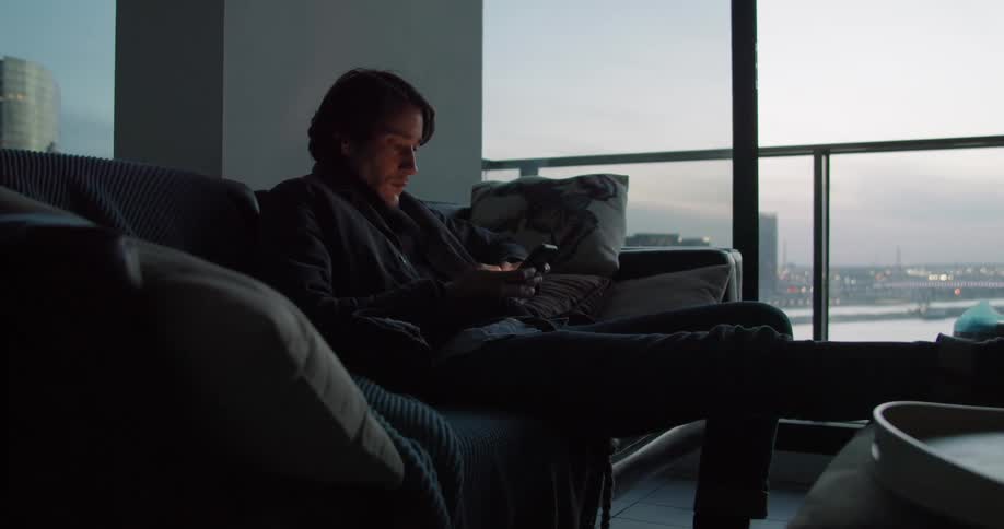 A man is sitting on a couch texting on his phone
