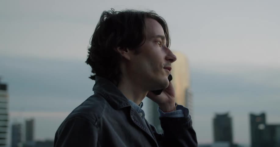 Young man speaking on his phone on a balcony near the city skyline