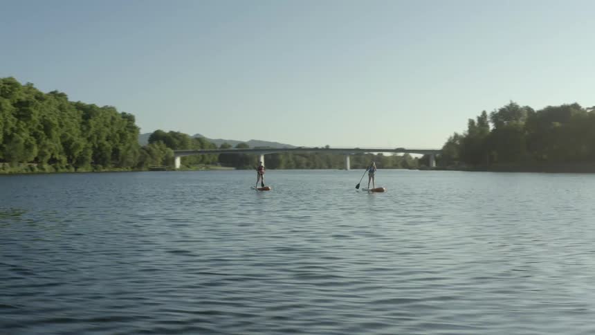 Two women standing on boards that are floating on the water using paddles to propel themselves through the water