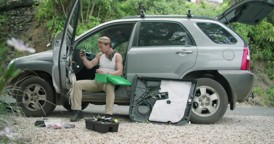 A man sits on the edge of his car seat and takes selfies