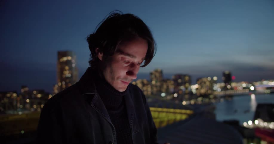 A man smiles while texting on the balcony of his downtown apartment