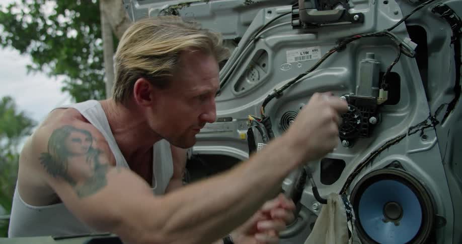 Blonde man with white undershirt and tattoo repairs car door