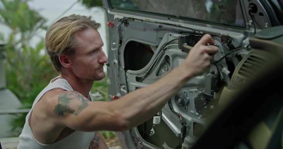 A man uses a torque wrench to unfasten a bolt from the inside of a car door