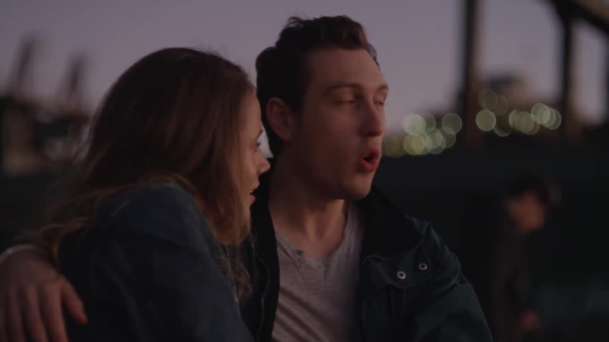 A man and woman sit outside talking at sunset