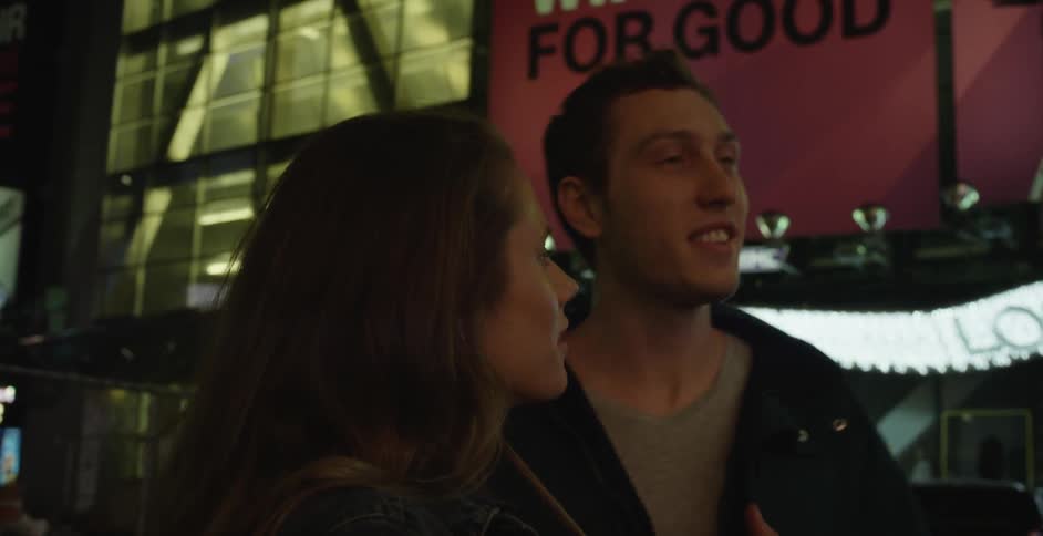 A man and woman look at a city and talk at night
