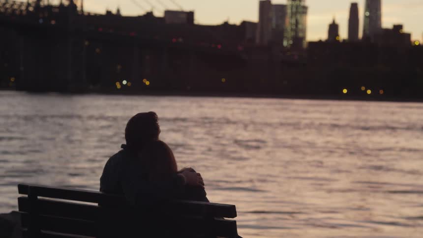 Two people are sitting together on a bench at dawn