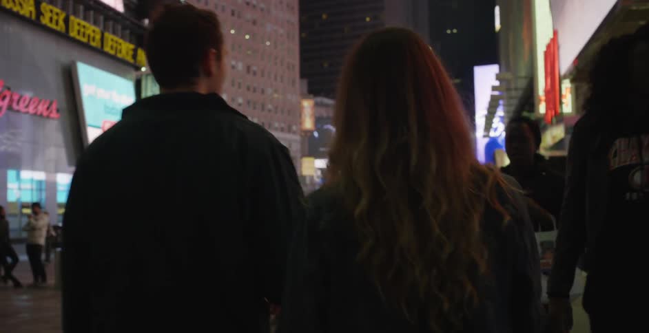 Man and woman walking in a city at night among other people