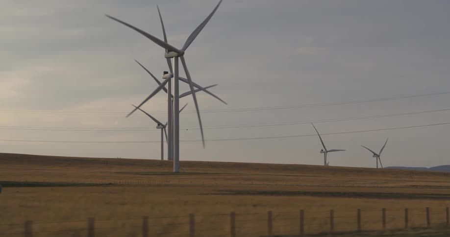 A landscape with a grassy field and wind turbines with the sky and clouds in the background