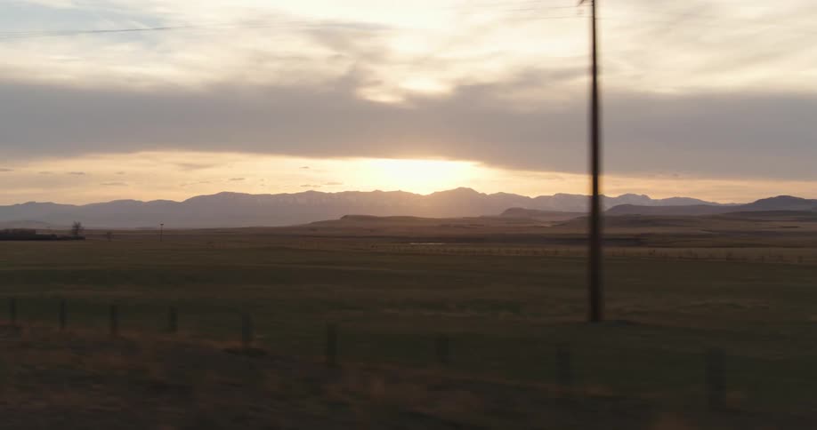 Sun shines from over mountains on horizon onto fenced pasture
