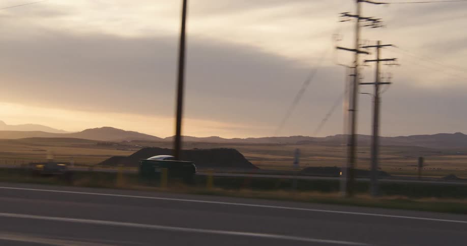 A white electric car is traveling on a desert road with mountains in the distance and the sun on the horizon