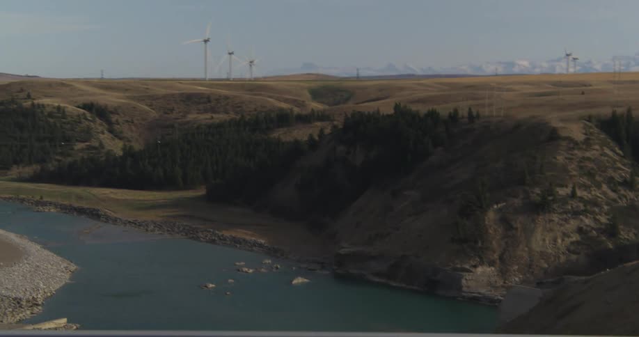 Wind turbines standing above a river visible from a bridge